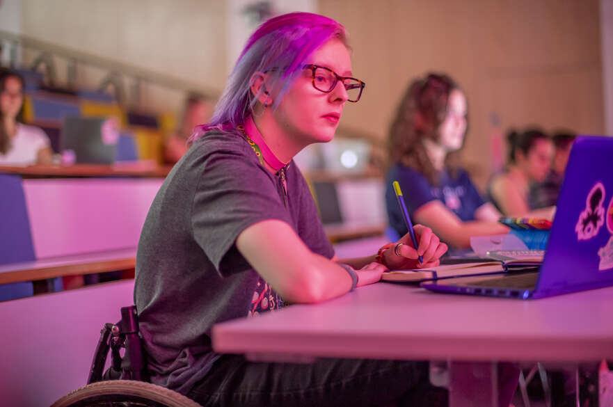 A female student in a wheelchair taking notes on her laptop in a lecture theatre